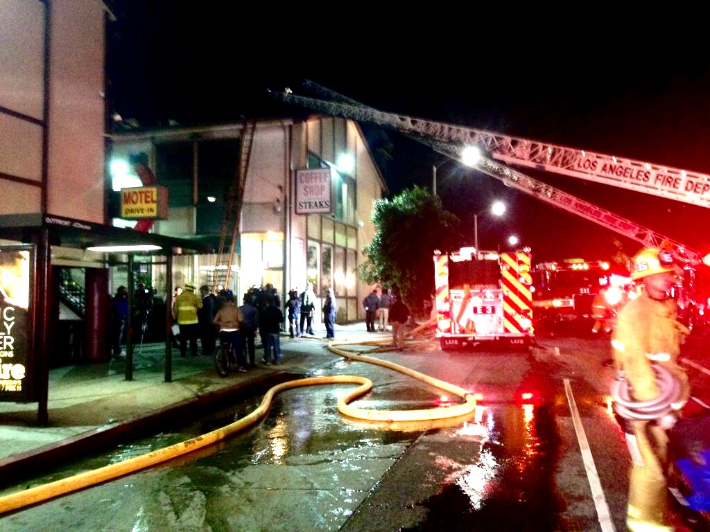 Fire Scene. Hose laid across wet pavement and truck ladders extended to burnt structure.