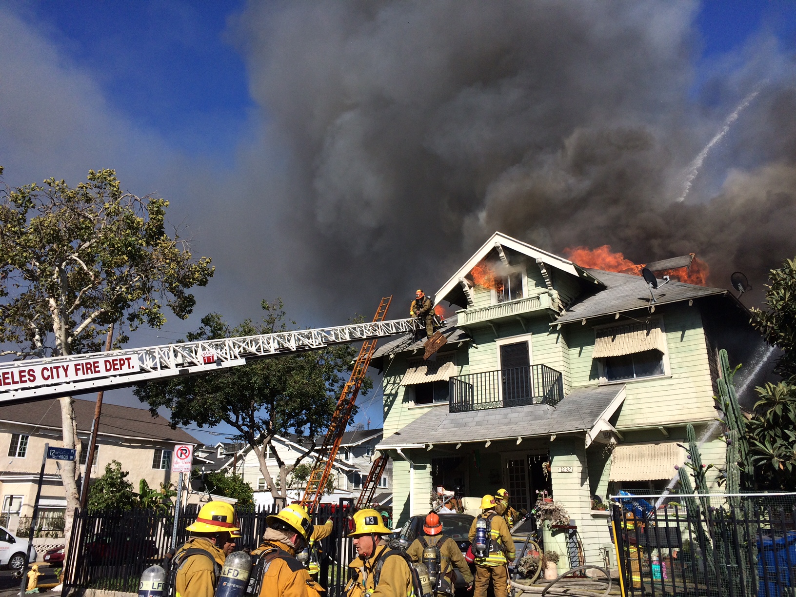 Large craftsman style home with heavy fire and firefighters climbing ladder