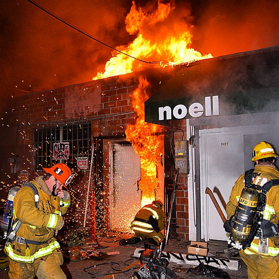 Three LAFD firefighters working in front of a burning structure.