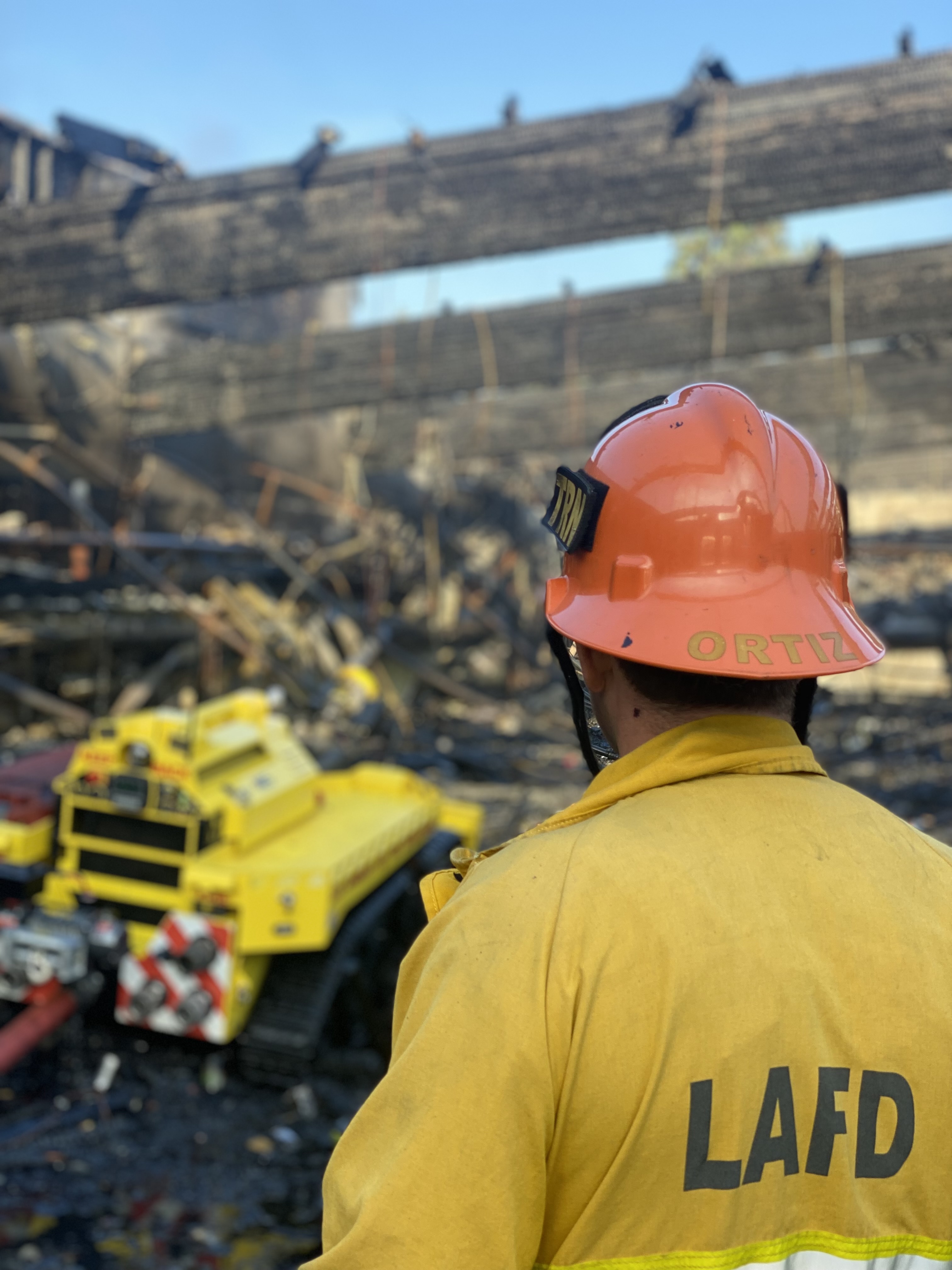 Foreground is firefighter using remote controls for the firefighting vehicle pictured in front of him