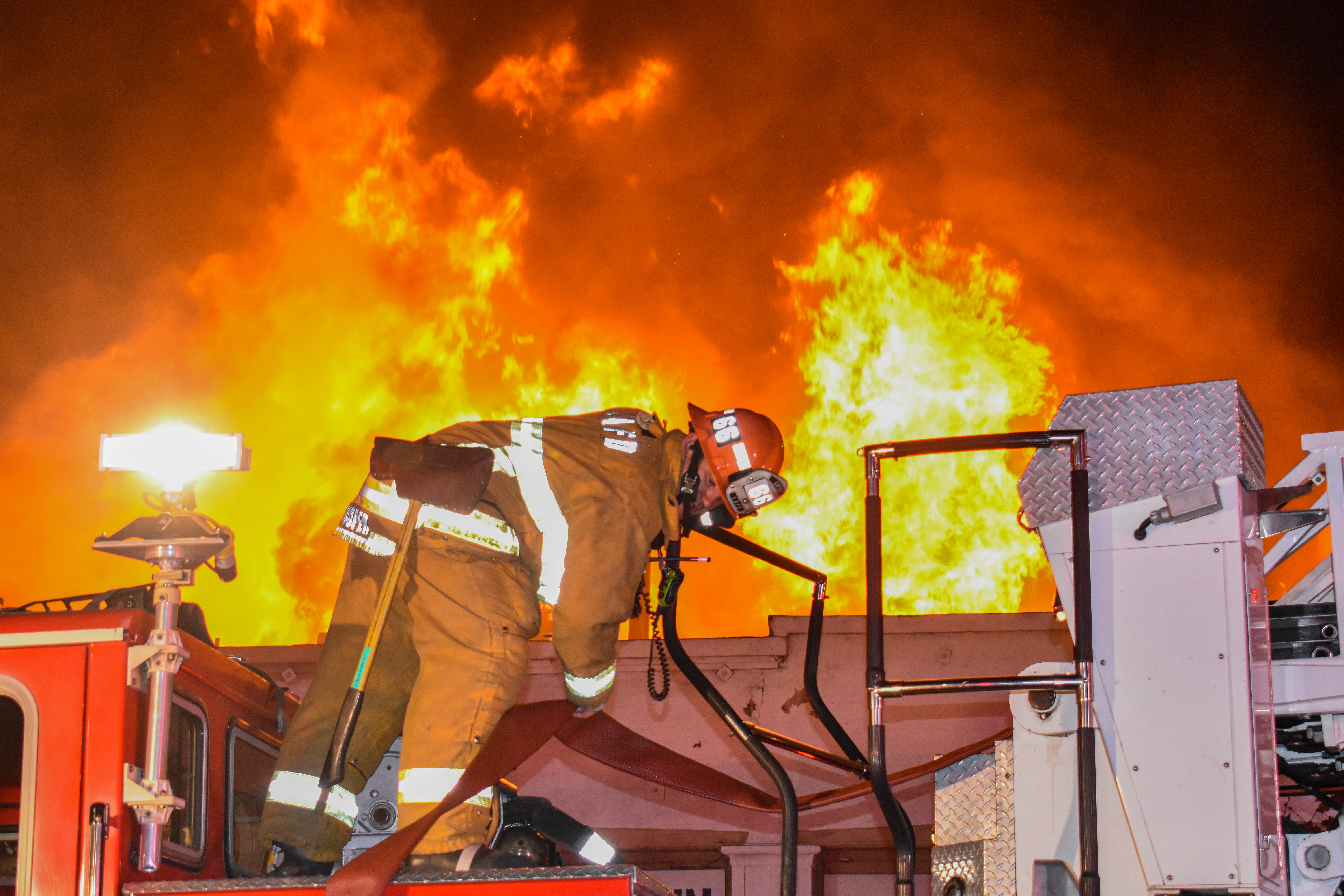 Firefighter on top of fire engine with large structure fire behind