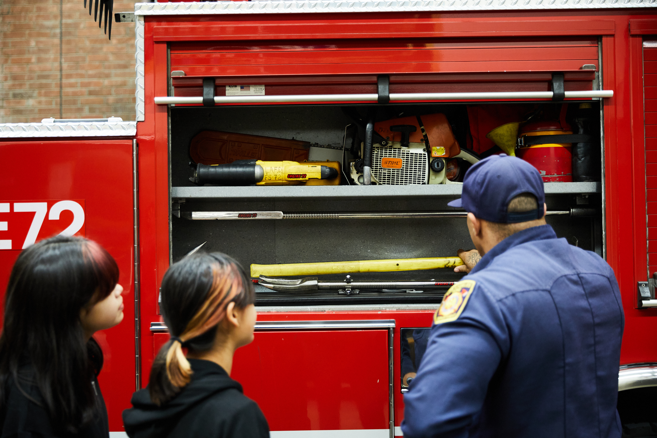 View from the back of firefighter explaining the contents of a compartment to the families