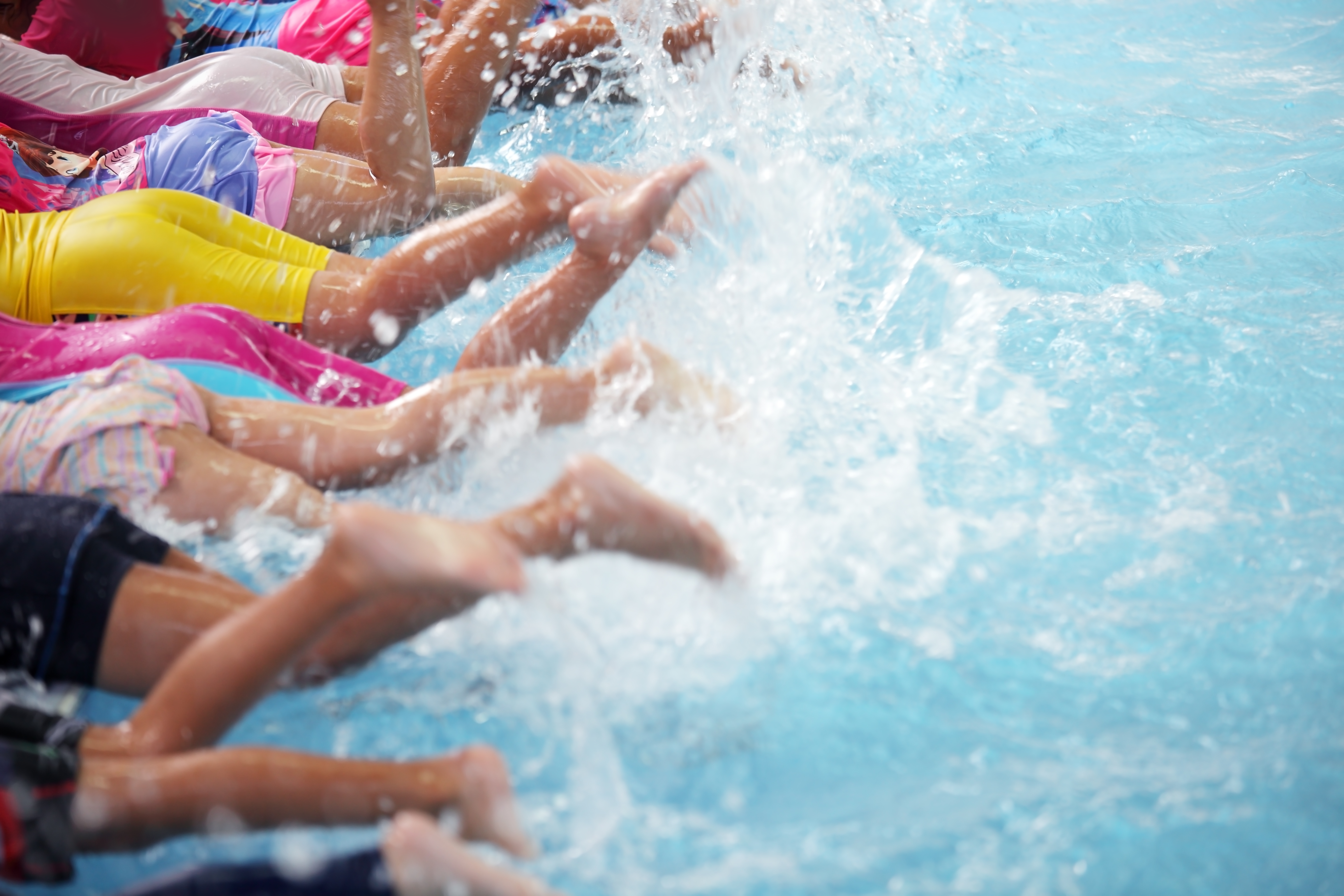 Row of children showing kicking feet in pool while learning to swim