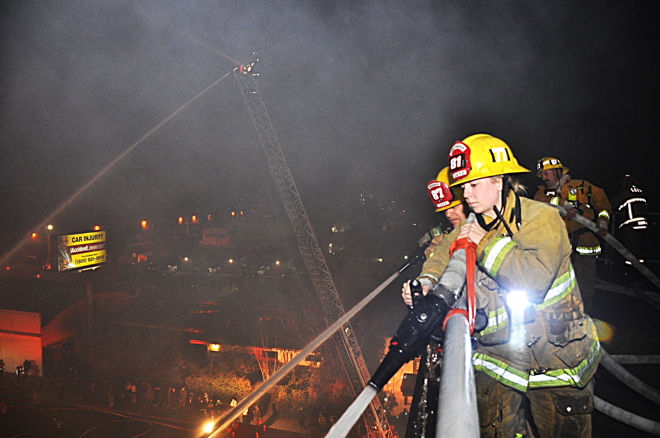 Firefighters seen on top of building with hose lines applying water to the fire below