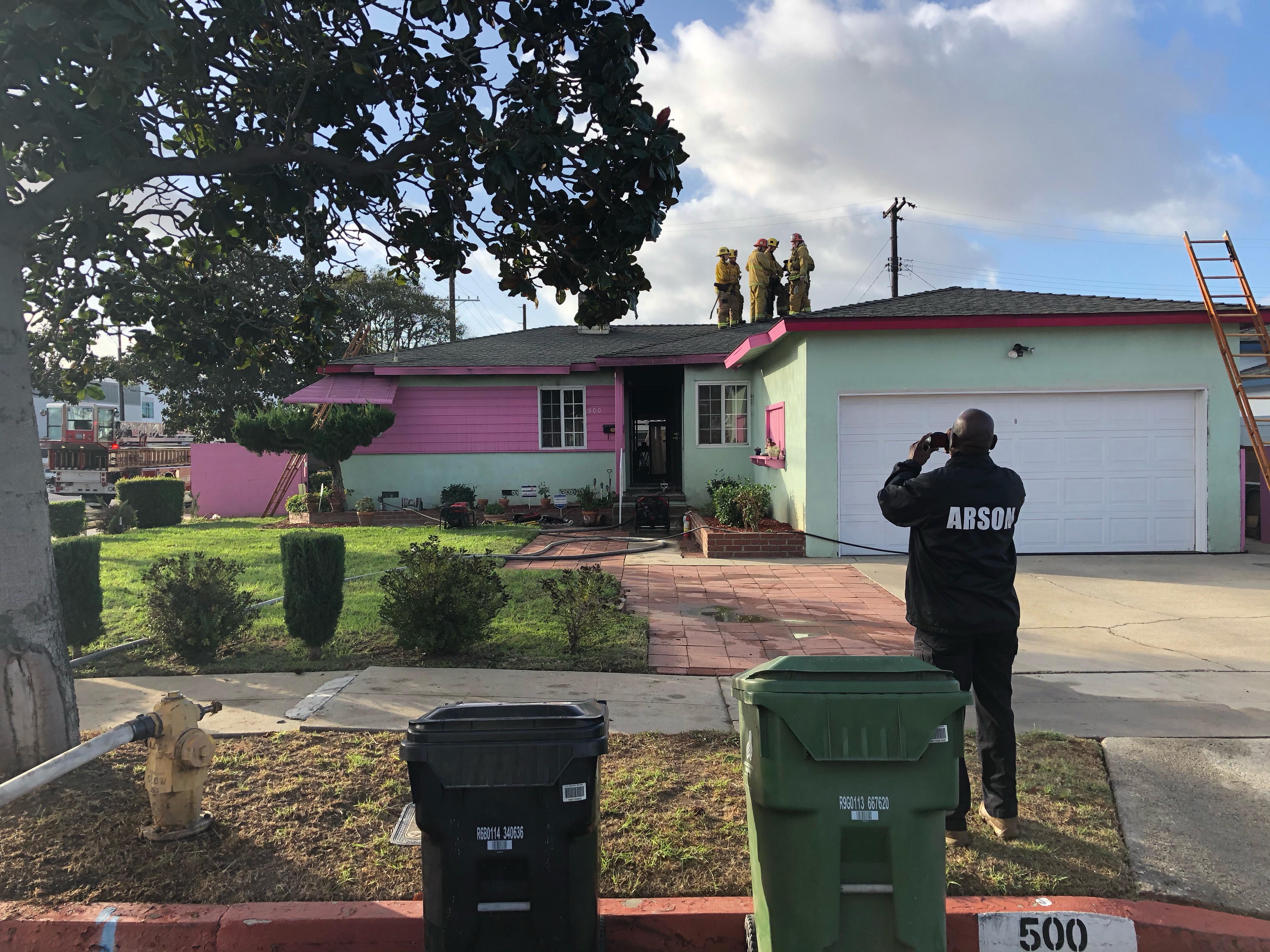 Arson investigator seen outside of structure taking a picture with firefighters visible on the roof